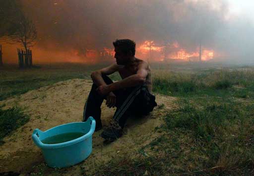 Мужчина сидит на земле у своего горящего дома под Выксой